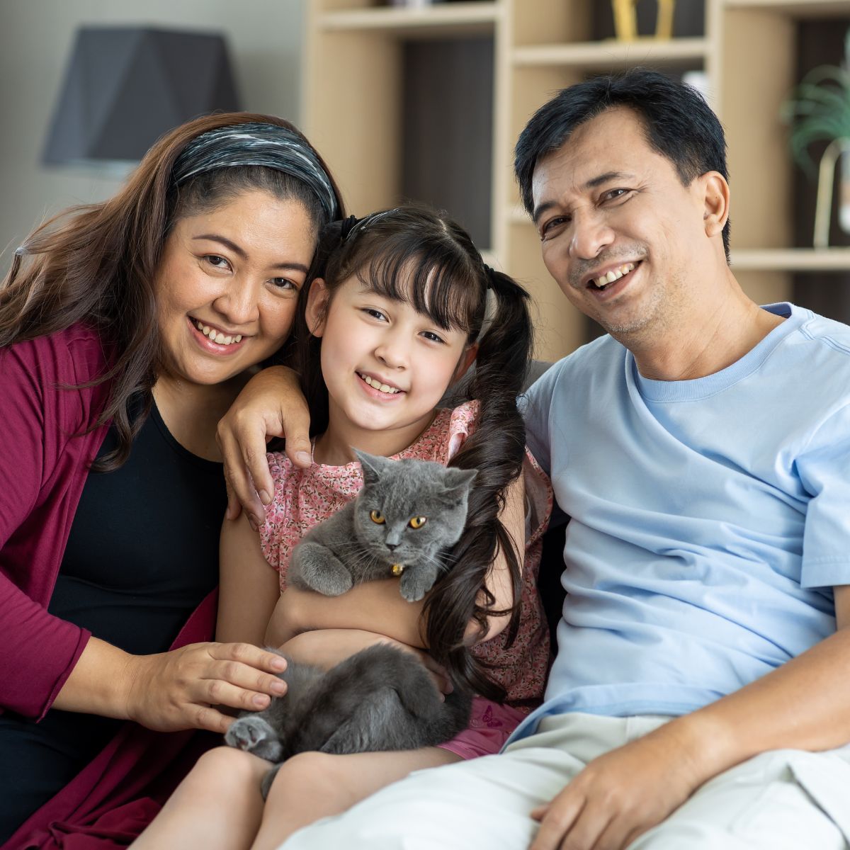 Family with their daughter holding a grey cat on the couch